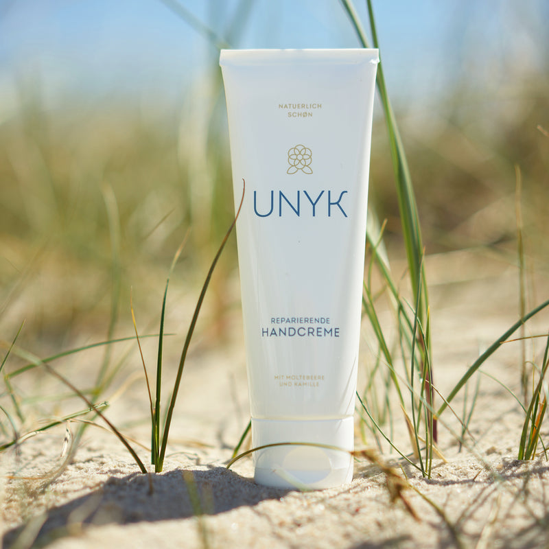 Handcreme von UNYK steht in den Dünen im Sand.